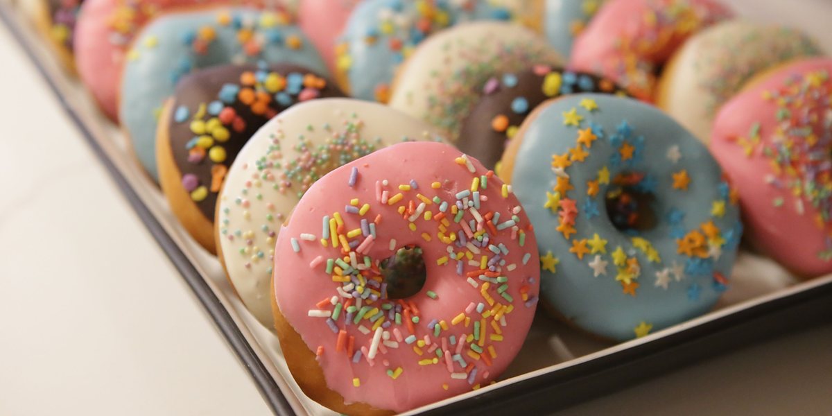 Licensed stock photograph: a full tray of iced ring donuts under coloured sprinkles